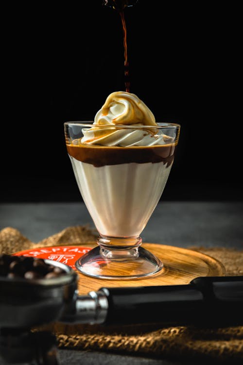 Free Delicious ice cream in glass decorated with whipped cream and caramel syrup on wooden tray near portafilter with coffee beans on table Stock Photo