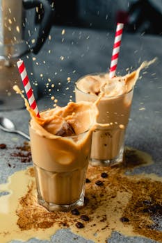 Exciting moment as iced coffee splashes from glass cups with striped straws on a rustic table.