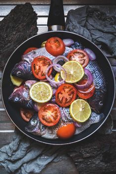 Colorful arrangement of fresh fish with lemon and tomato slices in a pan, ready for cooking.