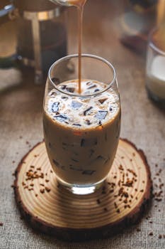 A refreshing iced coffee drink with coffee jelly served in a clear glass over a wooden coaster.