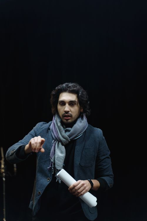 Free A male director in a dark theater, guiding rehearsals while holding a script. Stock Photo