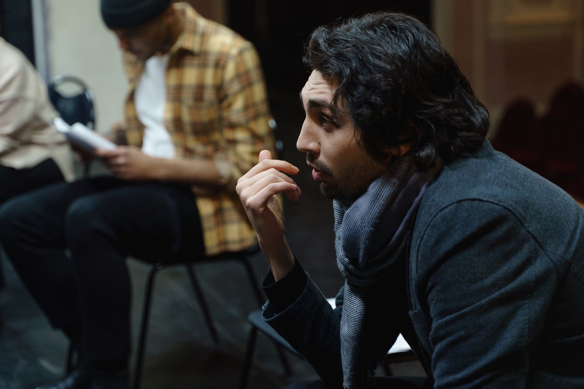Man attentively participates in a theater rehearsal, seated indoors, holding a script.