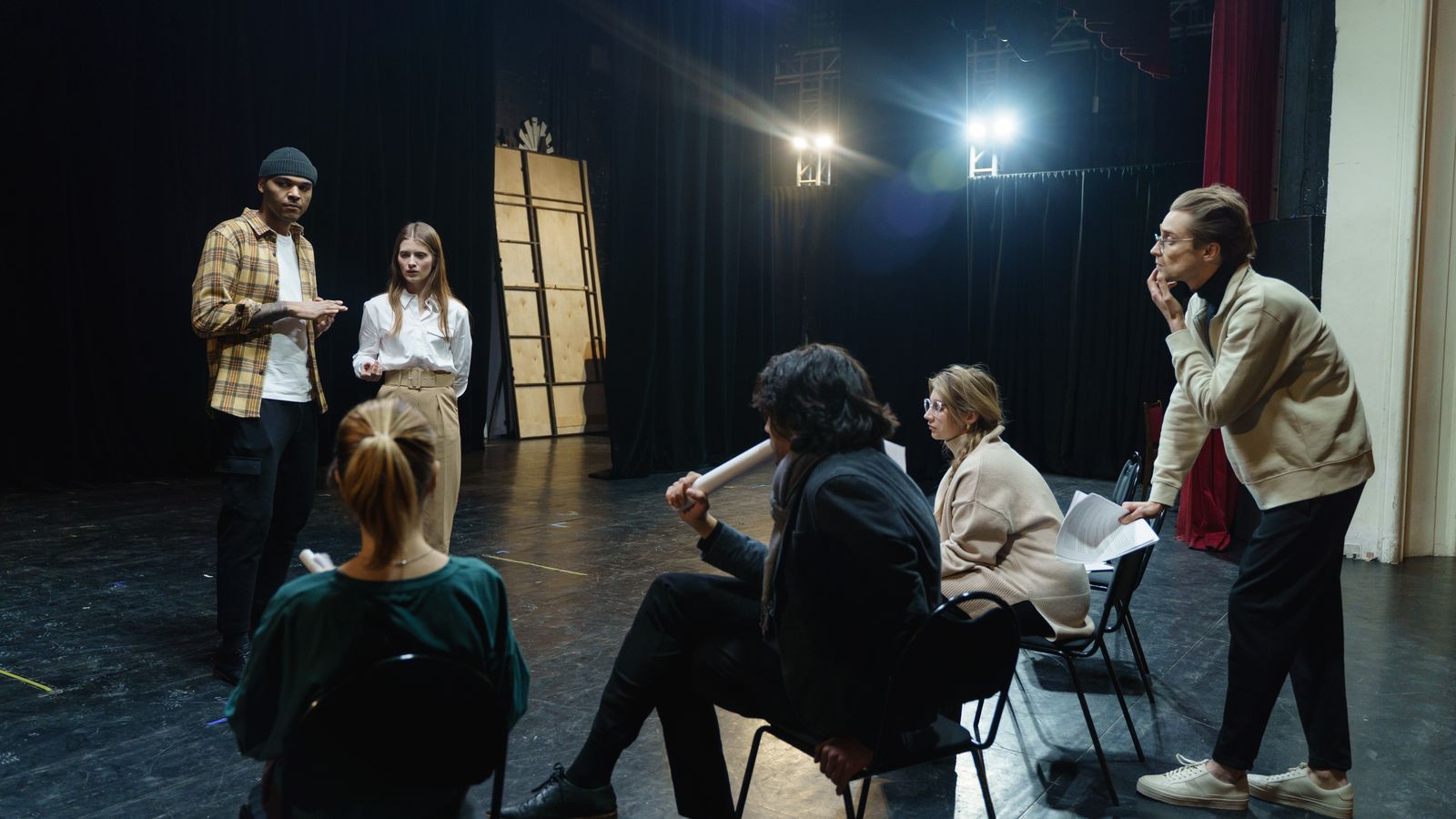 Adults standing and seated on a theatre stage with papers