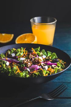 Bowl with tasty salad with green leaves and slices of onion and olives placed on black table near fork and glass of fresh orange juice