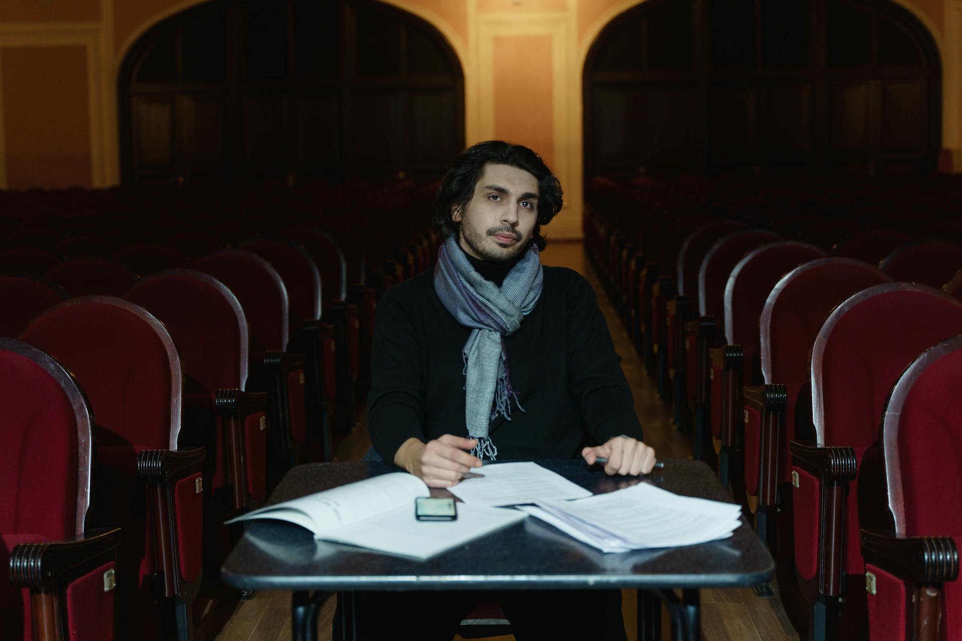 A theater director reviews scripts in an empty auditorium during a rehearsal preparation.