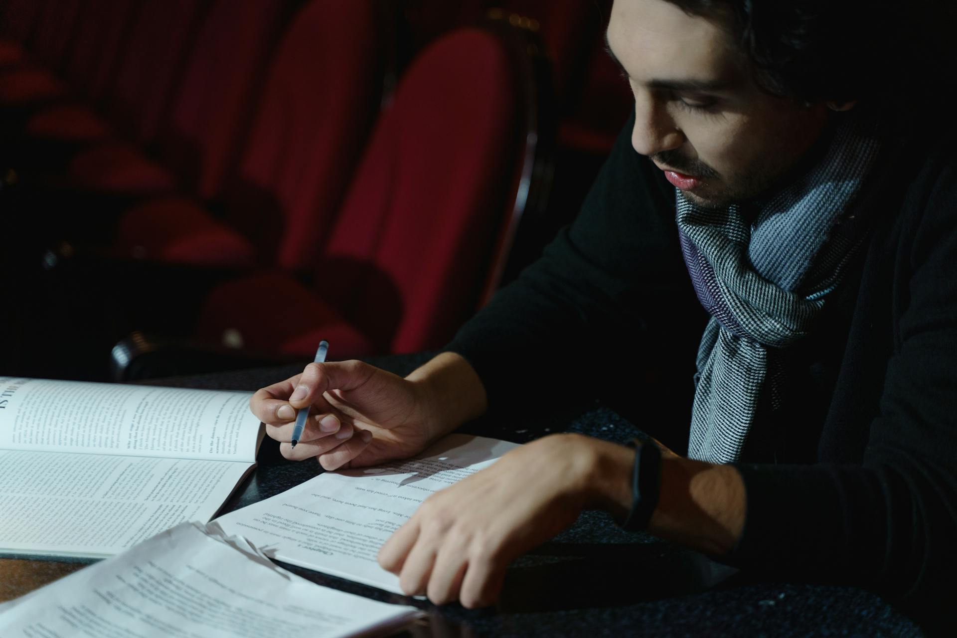 A theater director intensely reviewing a script in an auditorium during a rehearsal.