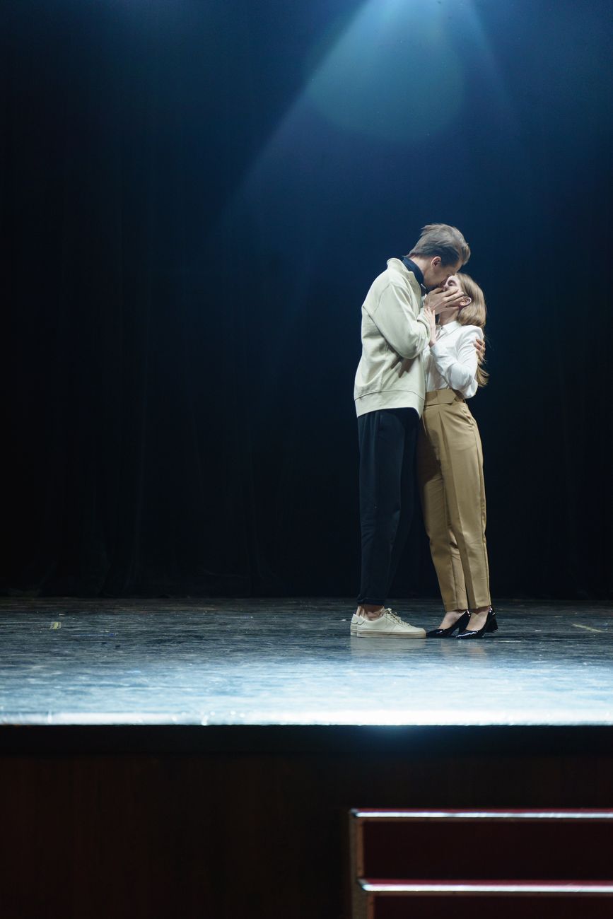 Een stel deelt een intiem moment op het podium onder dramatische verlichting.