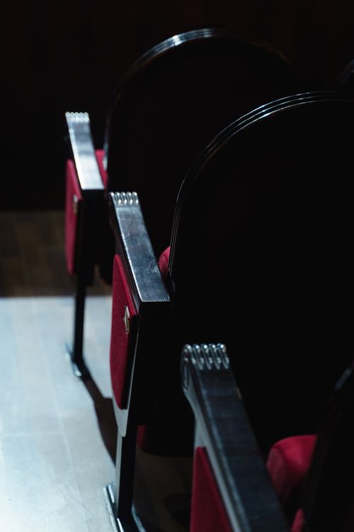 Free Vacant theater seats in soft lighting, highlighting plush red upholstery and black armrests. Stock Photo