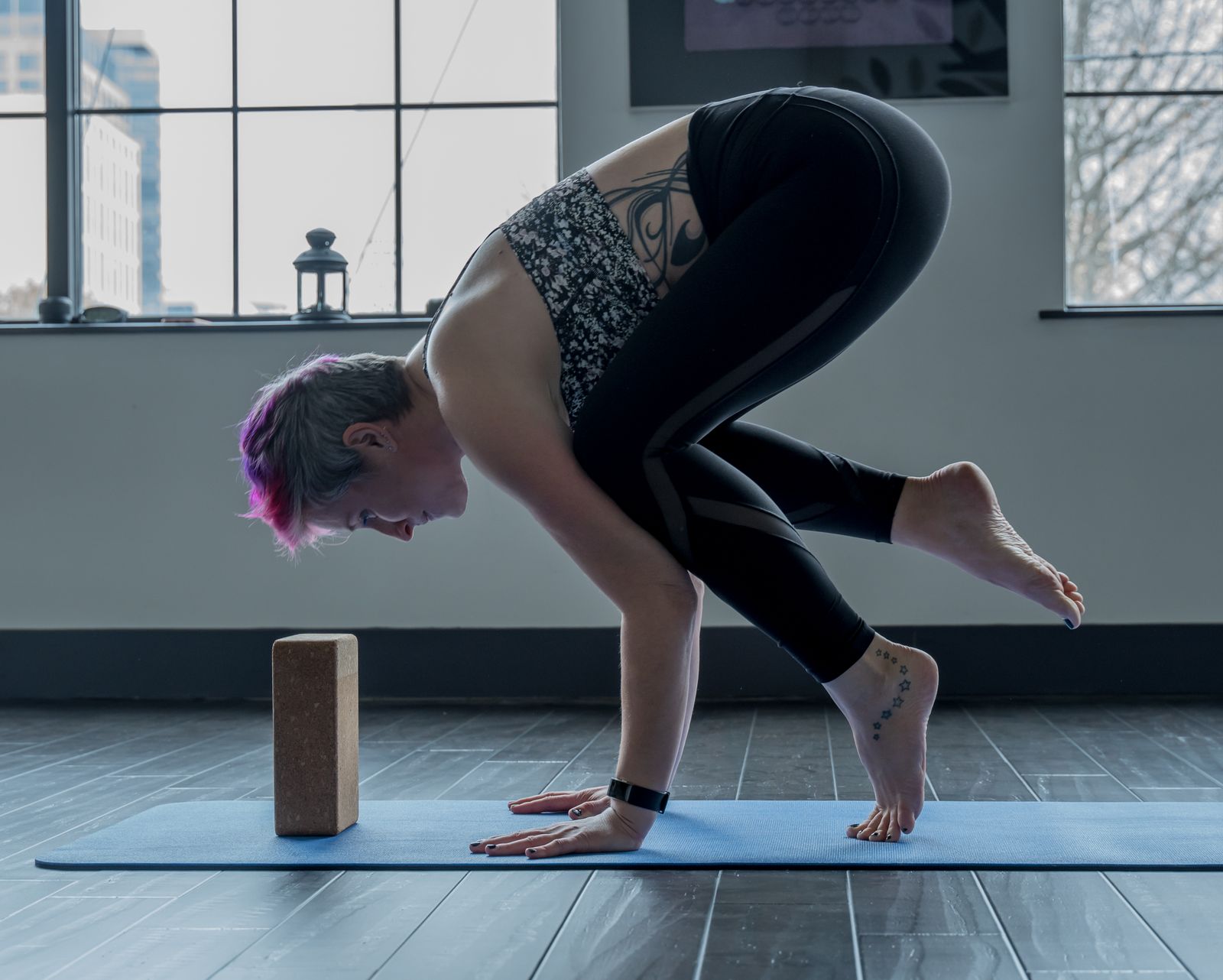 Woman practicing bakasana crow pose balanced on her hands on a yoga mat