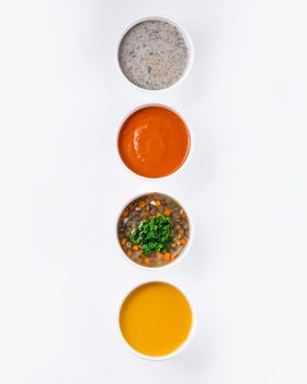 Top view of four diverse soups in white bowls on a white background.