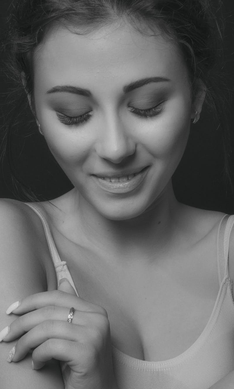 Monochrome portrait of a smiling young woman with eyes closed, exuding elegance.
