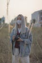 A Young Woman with Facemask and Wearing Denim Jacket Holding a Camera