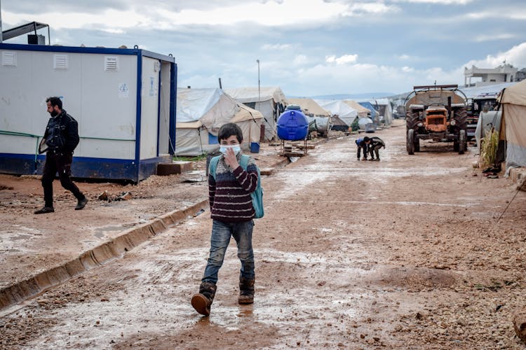 Ethnic Boy In Medical Mask Walking In Refugee Camp