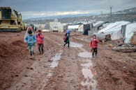 Poor children walking on muddy ground in settlement with tents