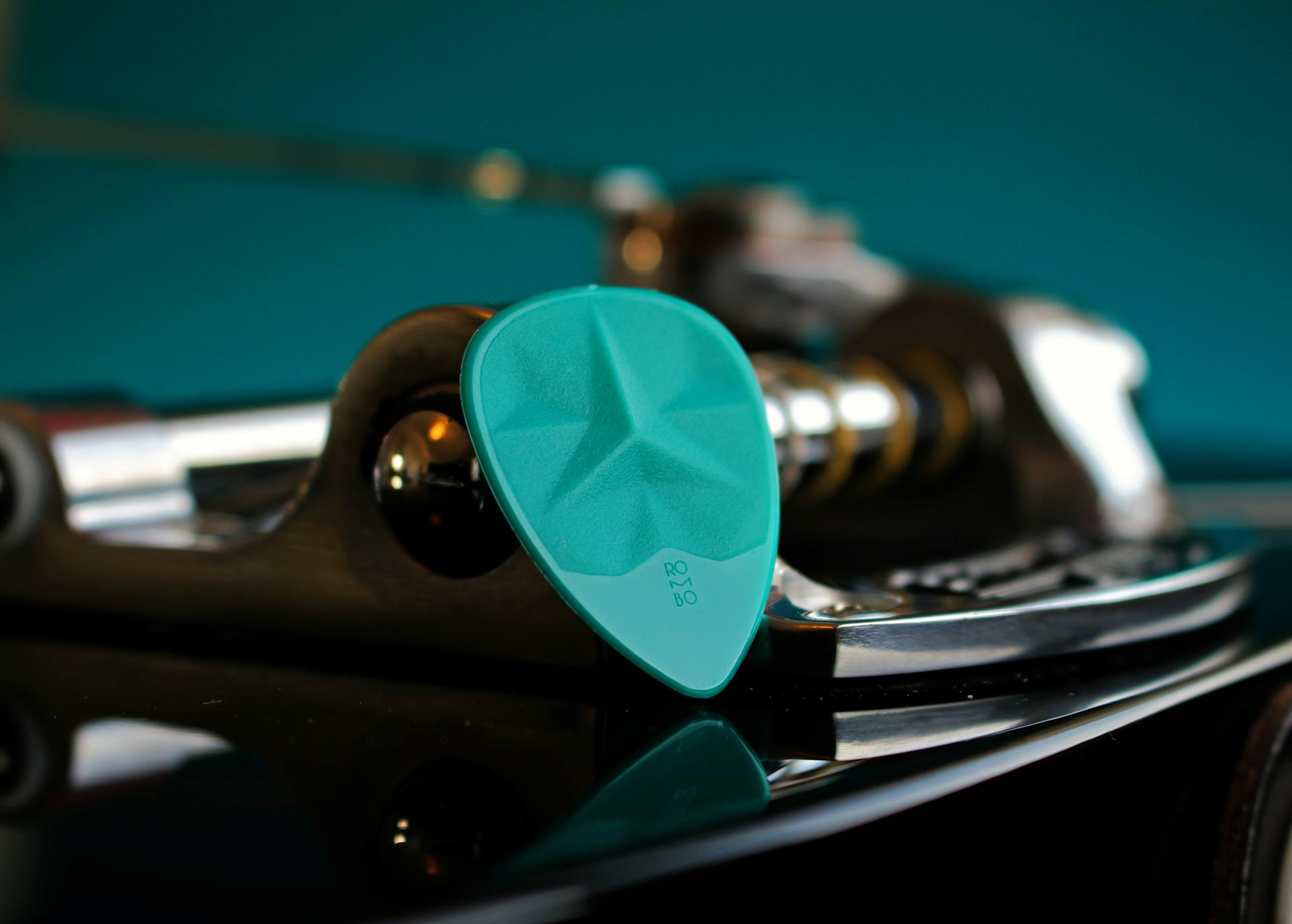 A close-up image of a turquoise guitar pick resting on an electric guitar.