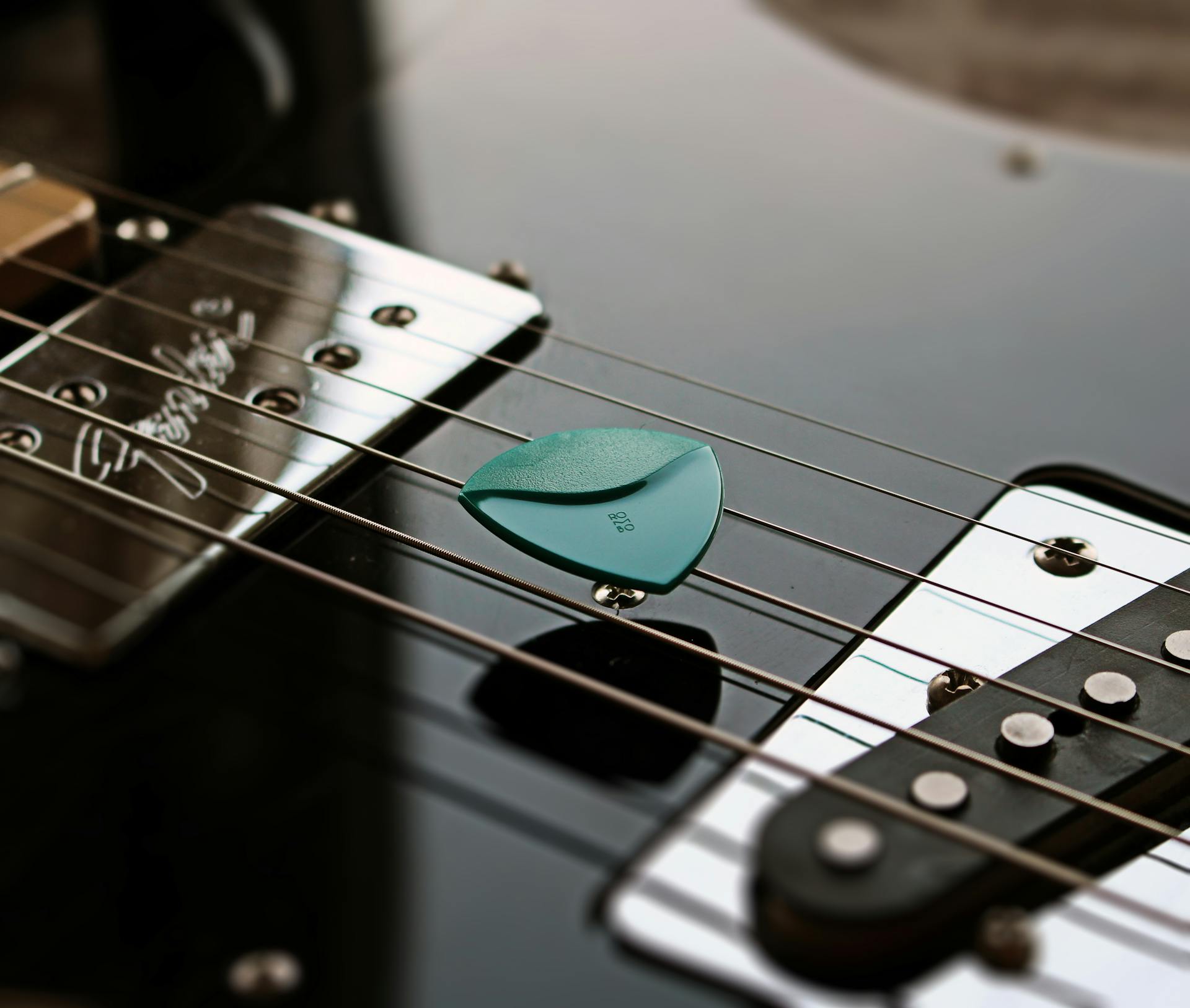 Close-up of a guitar pick resting on strings of an electric guitar, highlighting musical detail.
