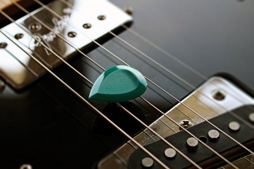 A detailed view of an electric guitar with a teal pick resting on its strings, showcasing texture and design.