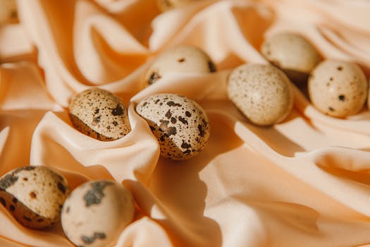 Elegant close-up of spotted quail eggs resting on soft peach-colored silk, showcasing delicate textures.