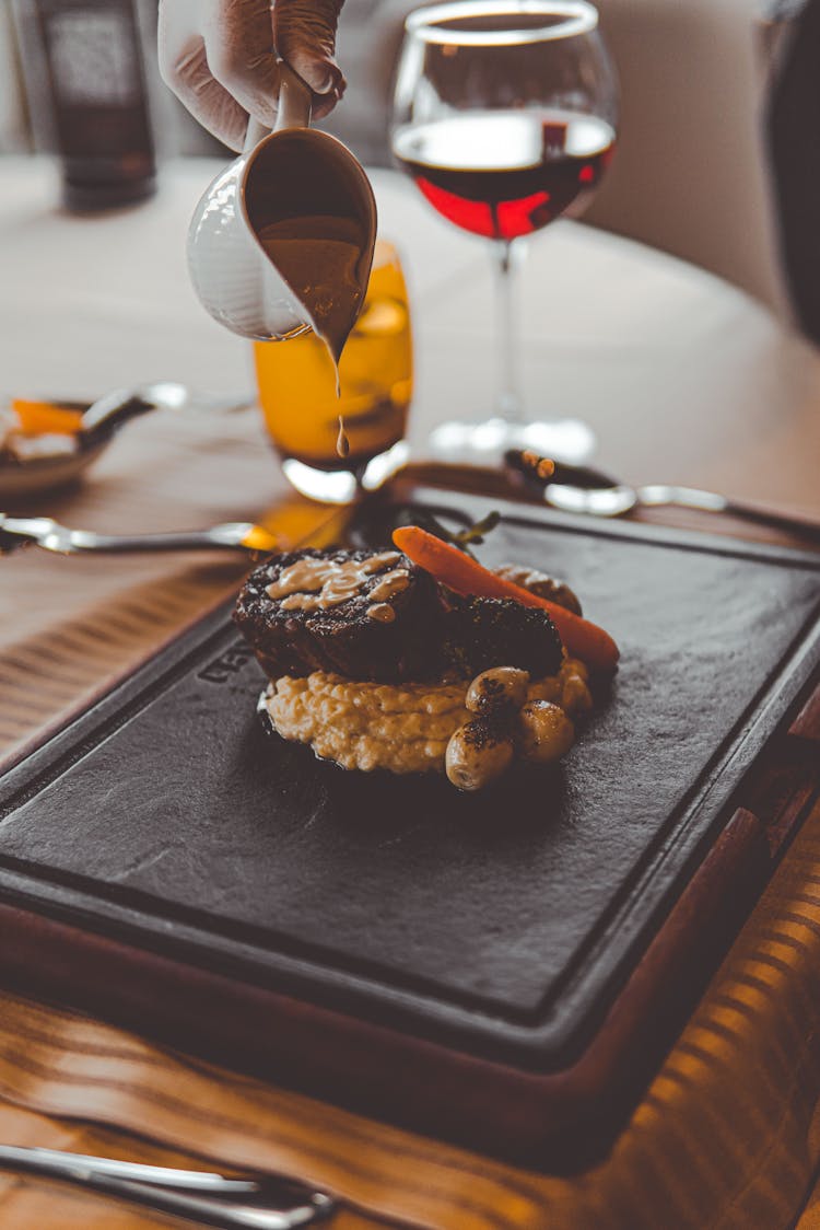 A Person Pouring Sauce On To The Steak