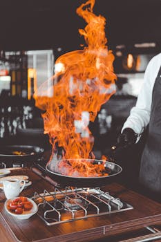 Chef skillfully handles a dramatic flame while cooking in a professional kitchen.