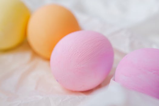 Vibrant pastel Easter eggs in pink, yellow, and orange on a soft fabric background, perfect for holiday decor.