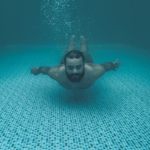 A Bearded Man Swimming Underwater in a Pool