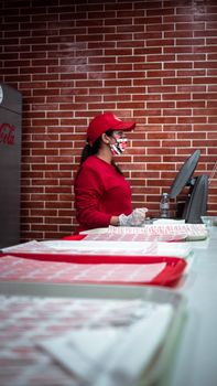 A fast food employee in a red uniform works at a counter in a Moroccan restaurant. Brick wall background.