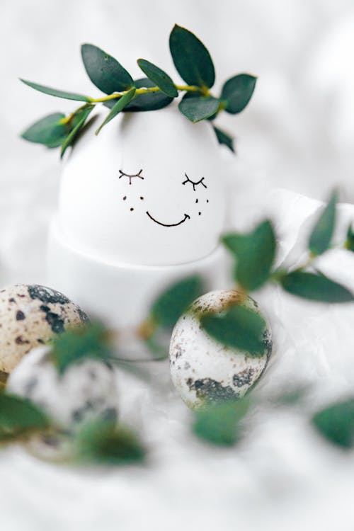 White Egg With Painted Face And Green Leaves