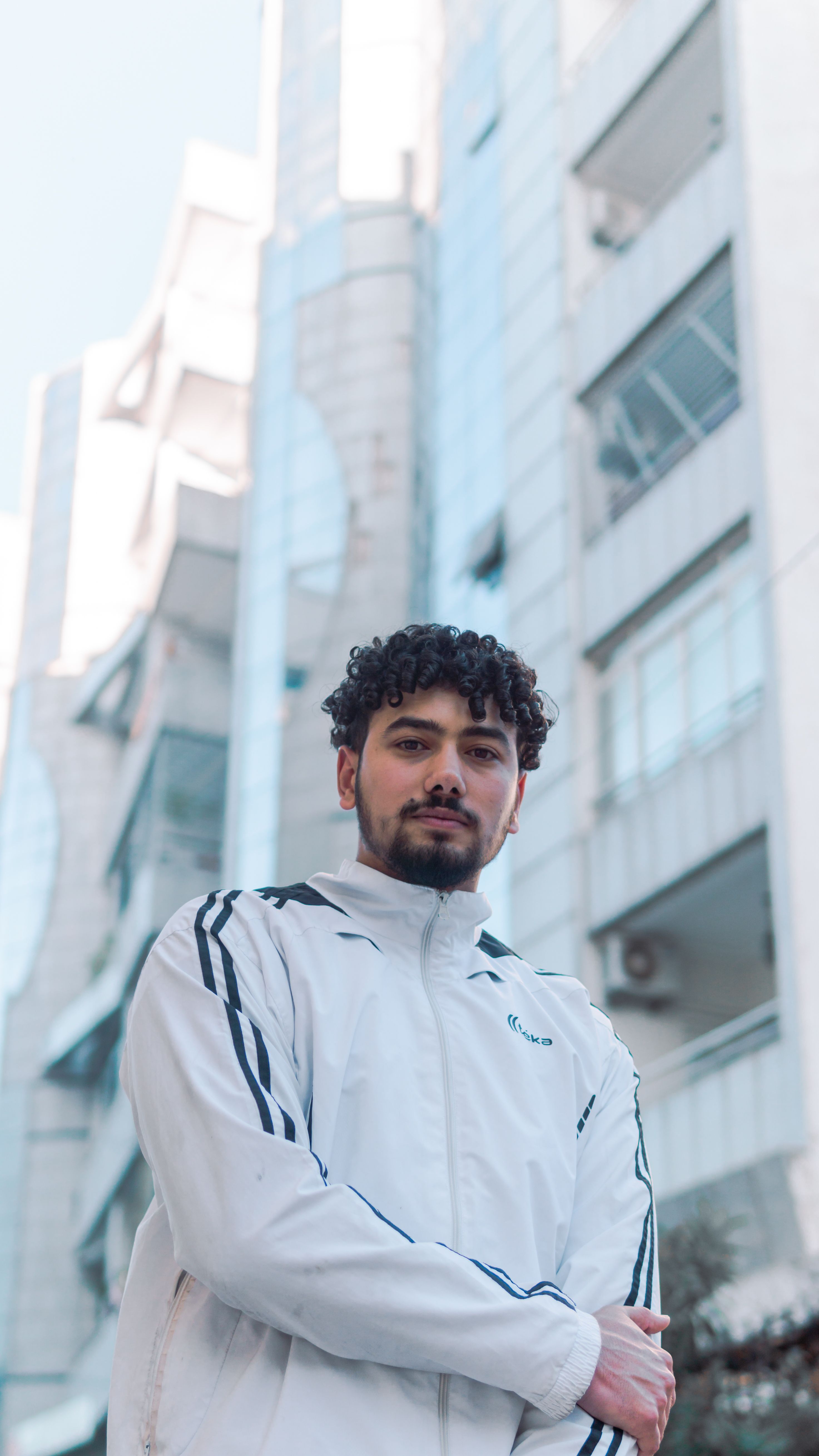 Man with curly hair and jacket stands confidently in front of a modern building in Fes, Morocco.