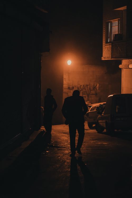 Free Two people silhouetted on a narrow street at night under a streetlight. Stock Photo