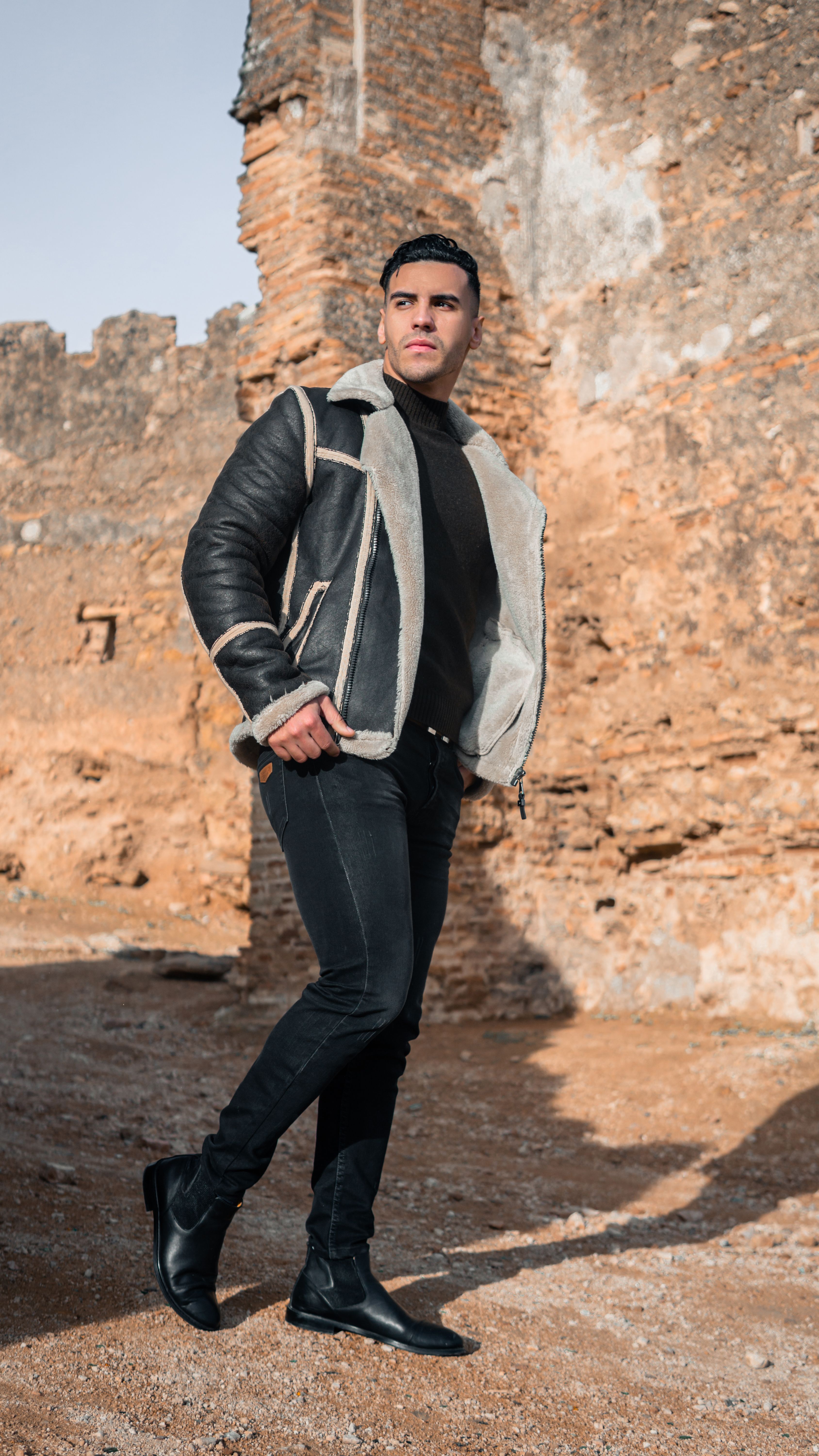 Fashionable man in black jacket posing against the ancient ruins in Fes, Morocco.