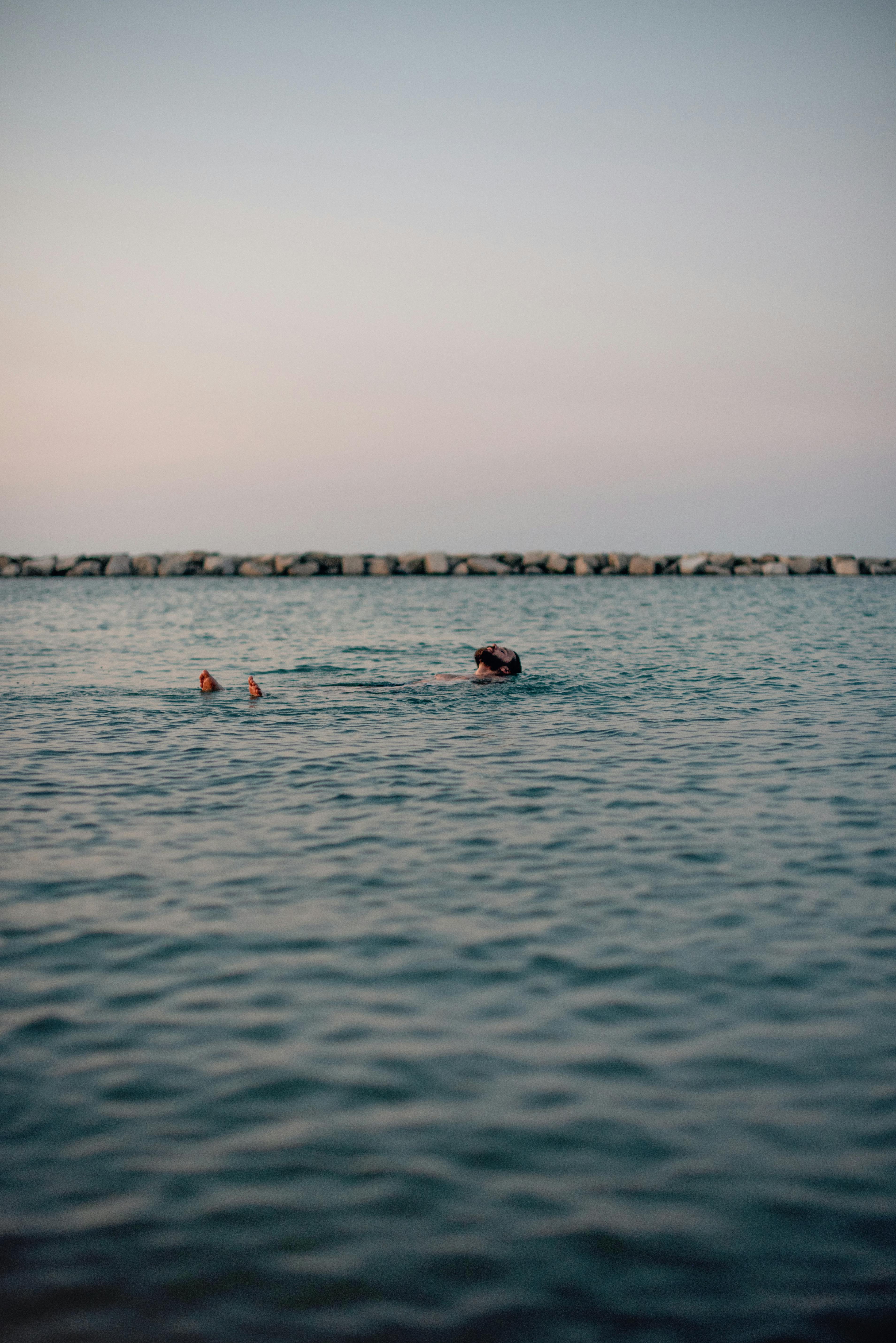 Tranquil scene of a person swimming in the ocean at dusk with soft ripples and a peaceful horizon.