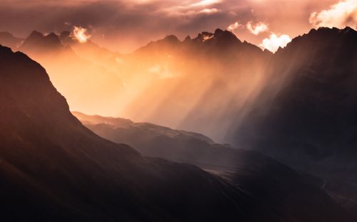 Free Stunning sunset over the misty Austrian Alps, highlighting dramatic sunbeams and rugged peaks. Stock Photo