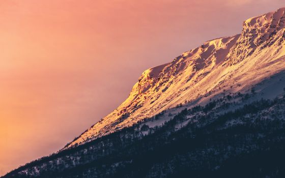 Captivating view of a snow-covered mountain peak at sunset in Norway with a warm, dramatic sky.