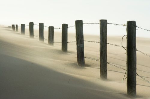 Free A scenic view of a barbed wire fence stretching across sandy dunes, with wind blowing sand. Stock Photo