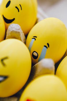 Close-up of yellow Easter eggs painted with emoji faces in an egg carton, showcasing creativity and fun.