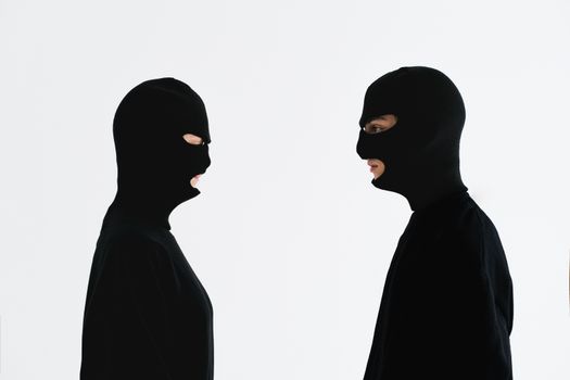 Two individuals in black balaclavas facing each other against a white background.
