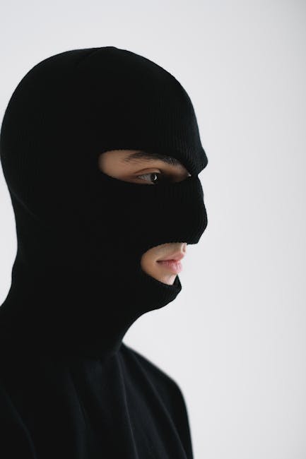 A side view portrait of a person wearing a black balaclava against a neutral background.