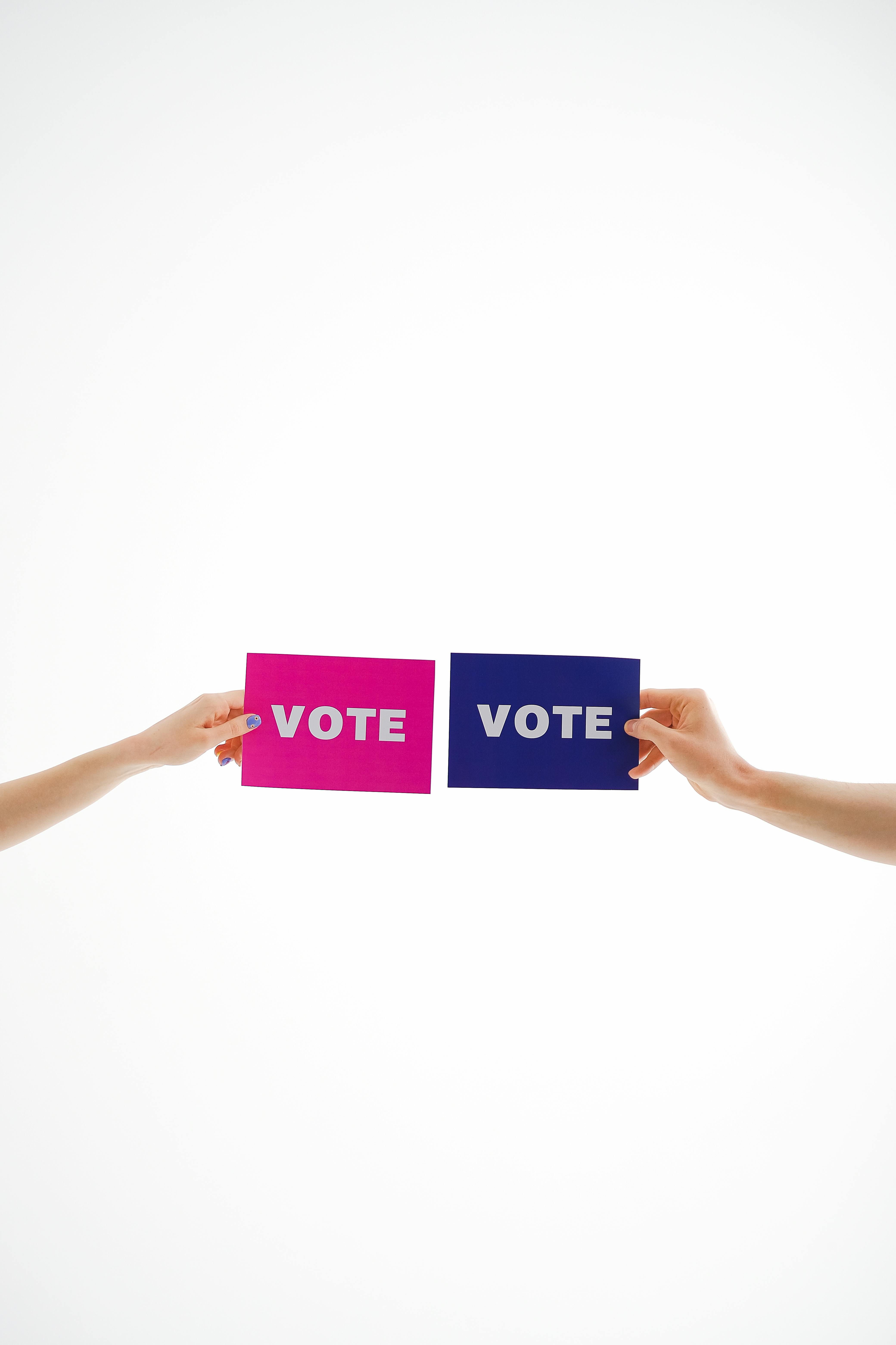Two hands holding vibrant vote cards against a white background promoting election awareness.
