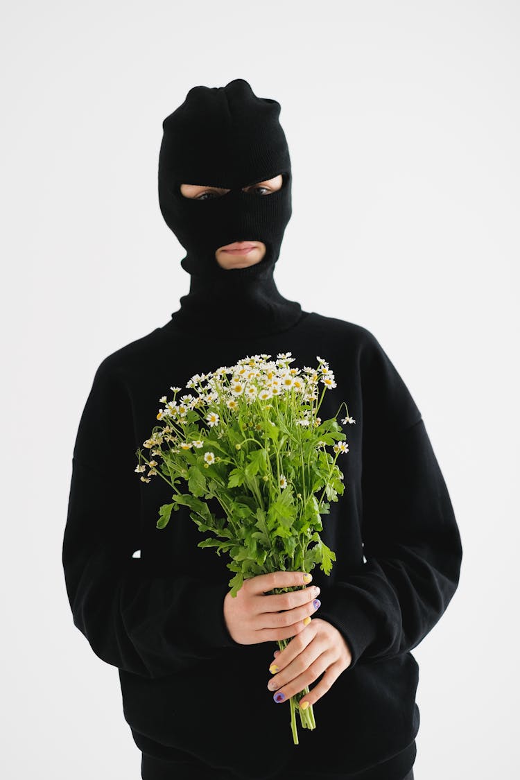 Man Wearing All Black And A Balaclava Holding A Bouquet