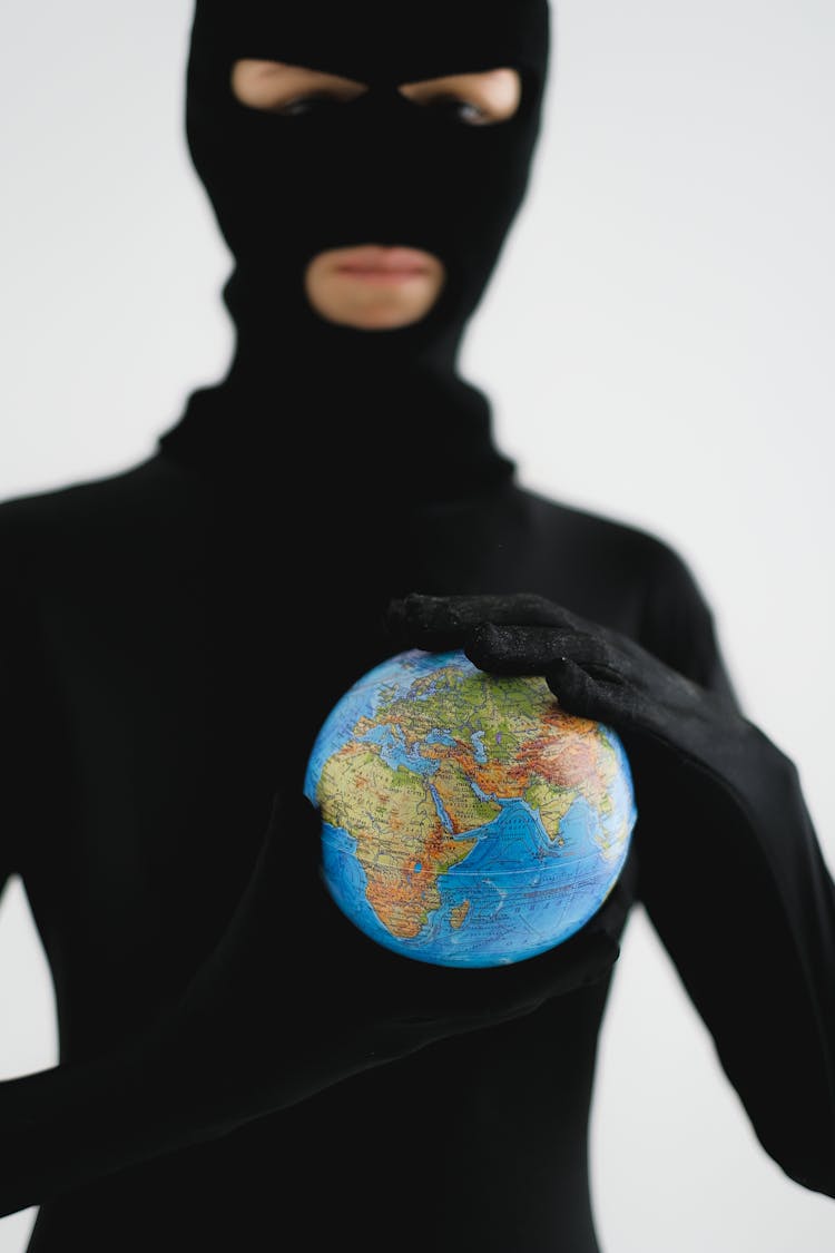 A Person In Black Robber Mask Holding A Globe