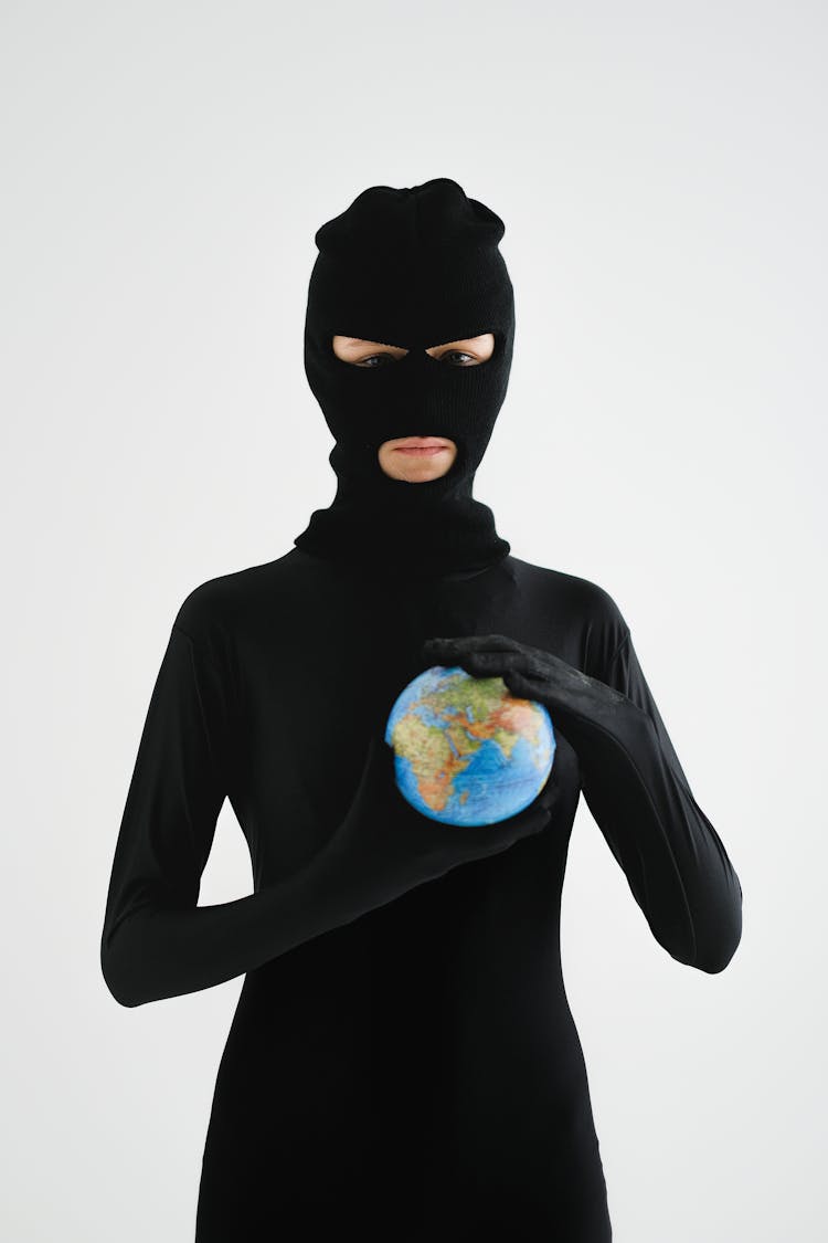 A Person In Black Robber Mask Holding A Globe