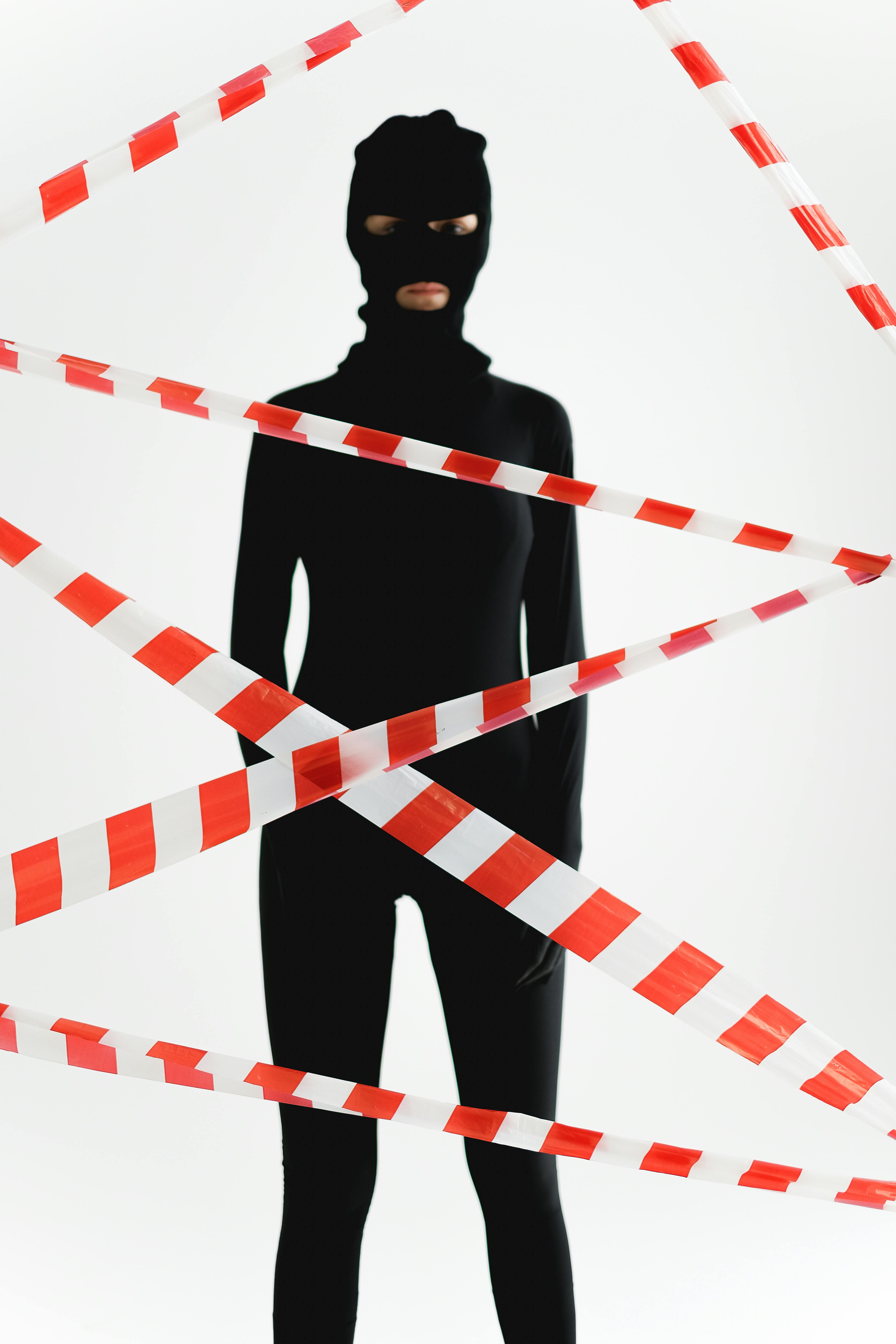 a person in black zentai suit standing behind red and white tape