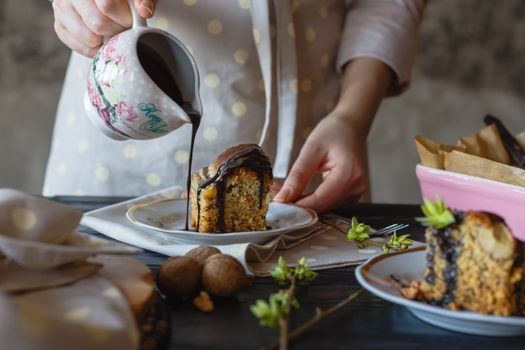 Delicious slice of nutty cake with chocolate syrup being poured over it, creating a mouthwatering dessert moment.