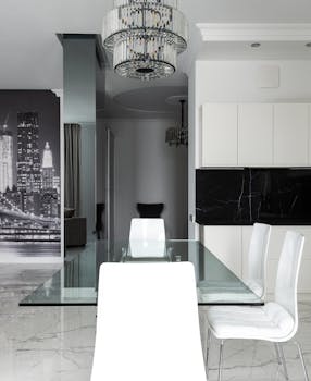 A sleek modern dining room featuring a glass table, white chairs, and a monochrome cityscape mural.