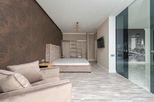 Interior of apartment with armchair next to bed in front of TV on wall near glass door