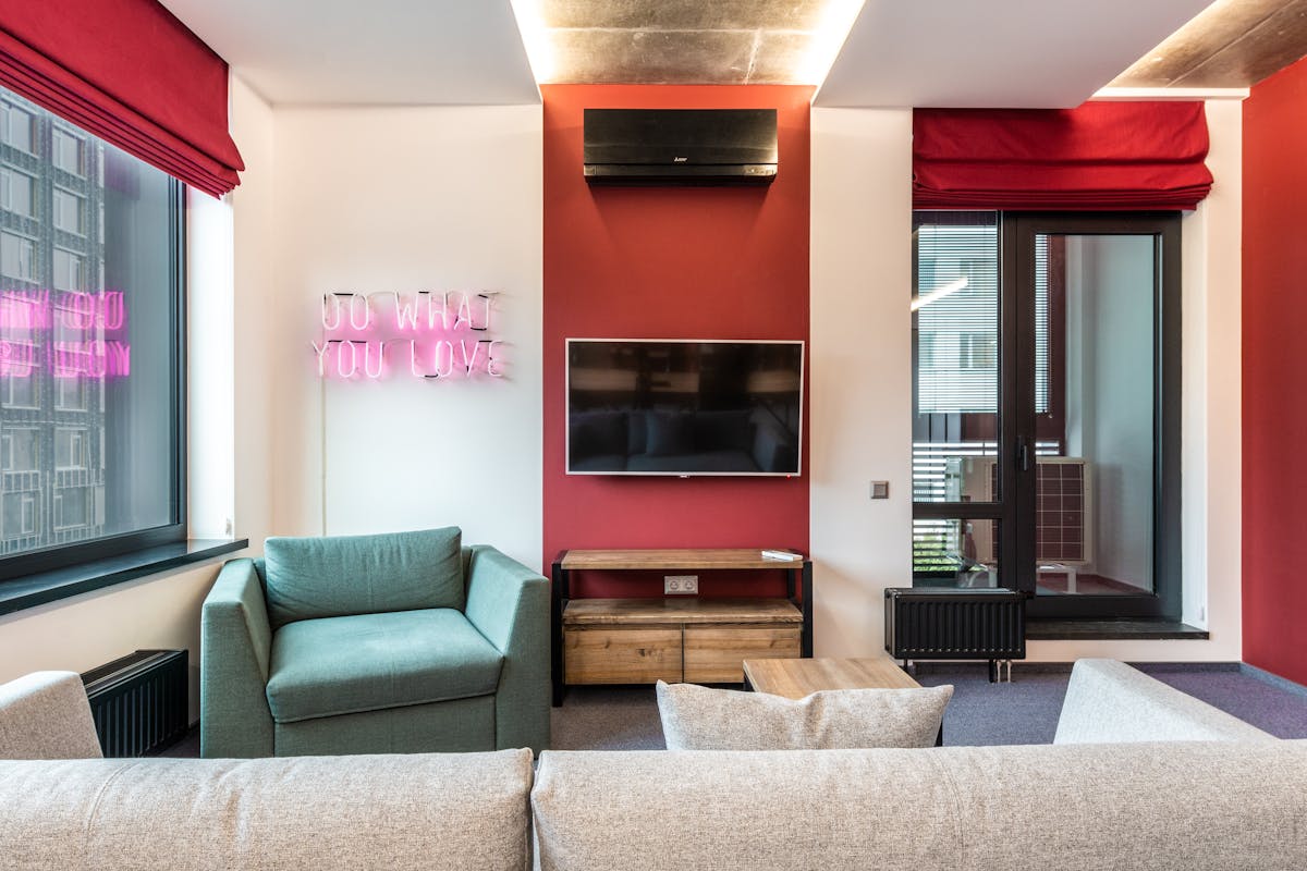 Interior of modern office lounge zone with sofa and armchair with table near window next to TV on wall and neon signboard with text do what you love near door