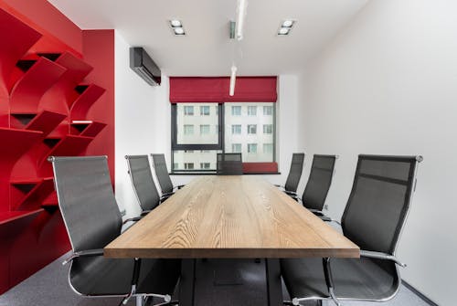 Interior of modern conference room with wooden table and chairs next to red shelves near window with jalousie