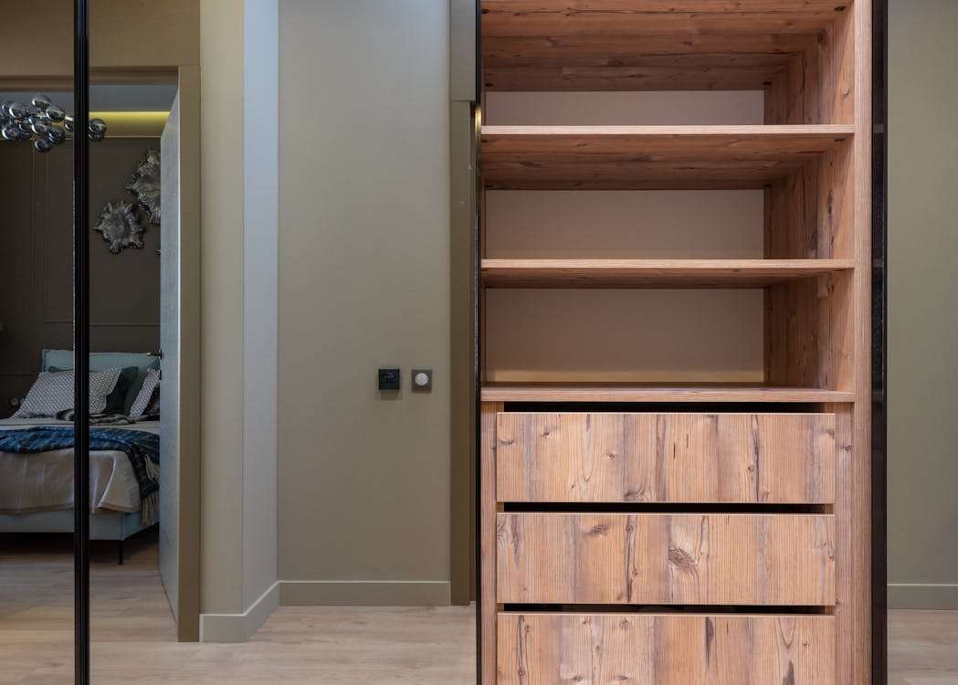 Free Interior Of Light Apartment With Wooden Cabinet With Empty Shelves Next To Bed Stock Photo