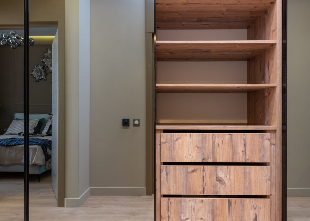 Quarto claro com cama ao lado de armário alto com prateleiras e gavetas